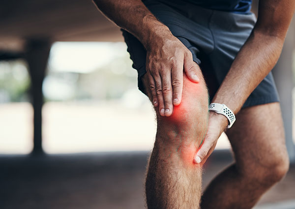Knochenmarkoedemtherapie im Zentrum für Mobilität in Wien - Sportler fast sich an sein gerötetes Knie und hat sichtlich Schmerzen