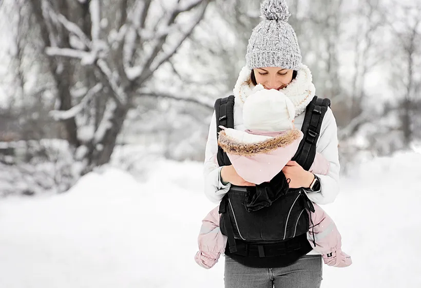 Baby schläft in Babytrage auf der Brust der Mama im Winter draußen