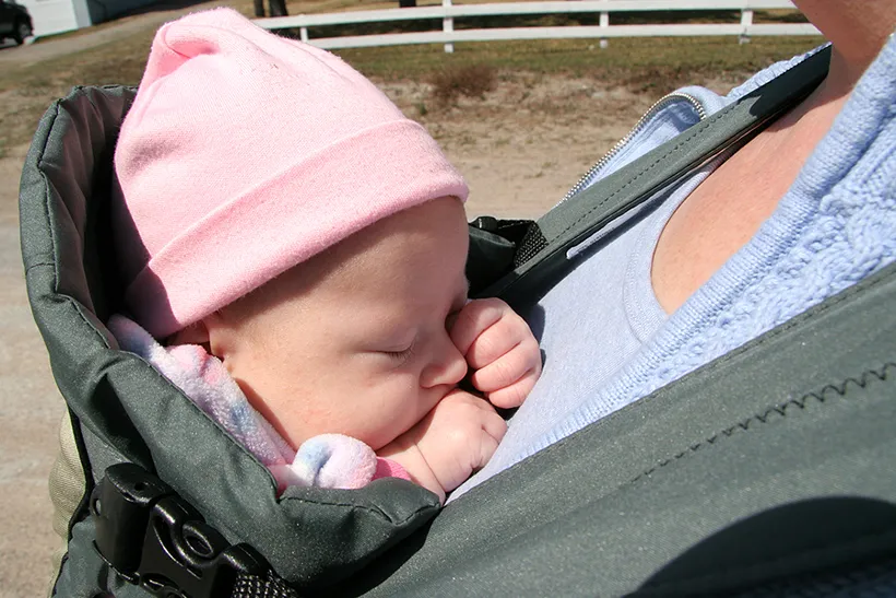 Baby schläft in Babytrage auf der Brust der Mama